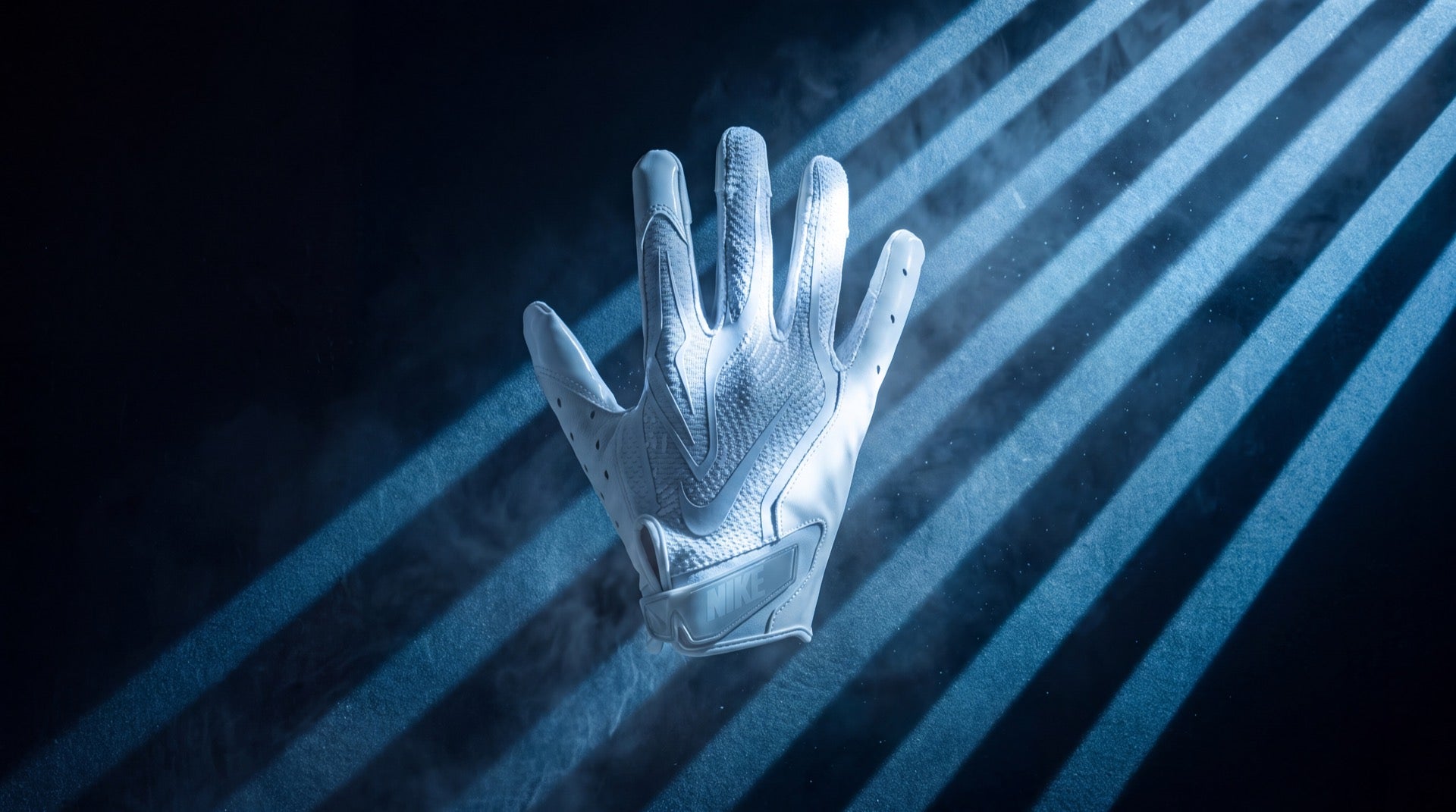 White Nike Vapor Jet 9.0 football glove floating in cold blue gobo light with drifting mist