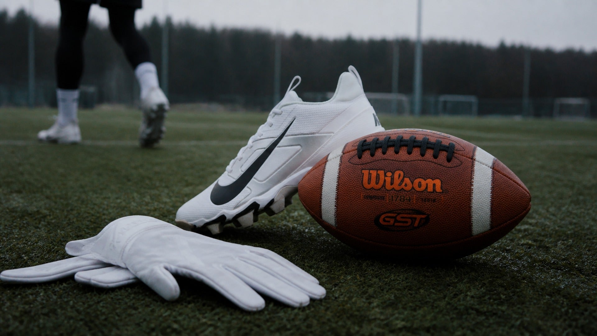 Flag football equipment on a field with a Wilson football, white gloves and Nike cleats